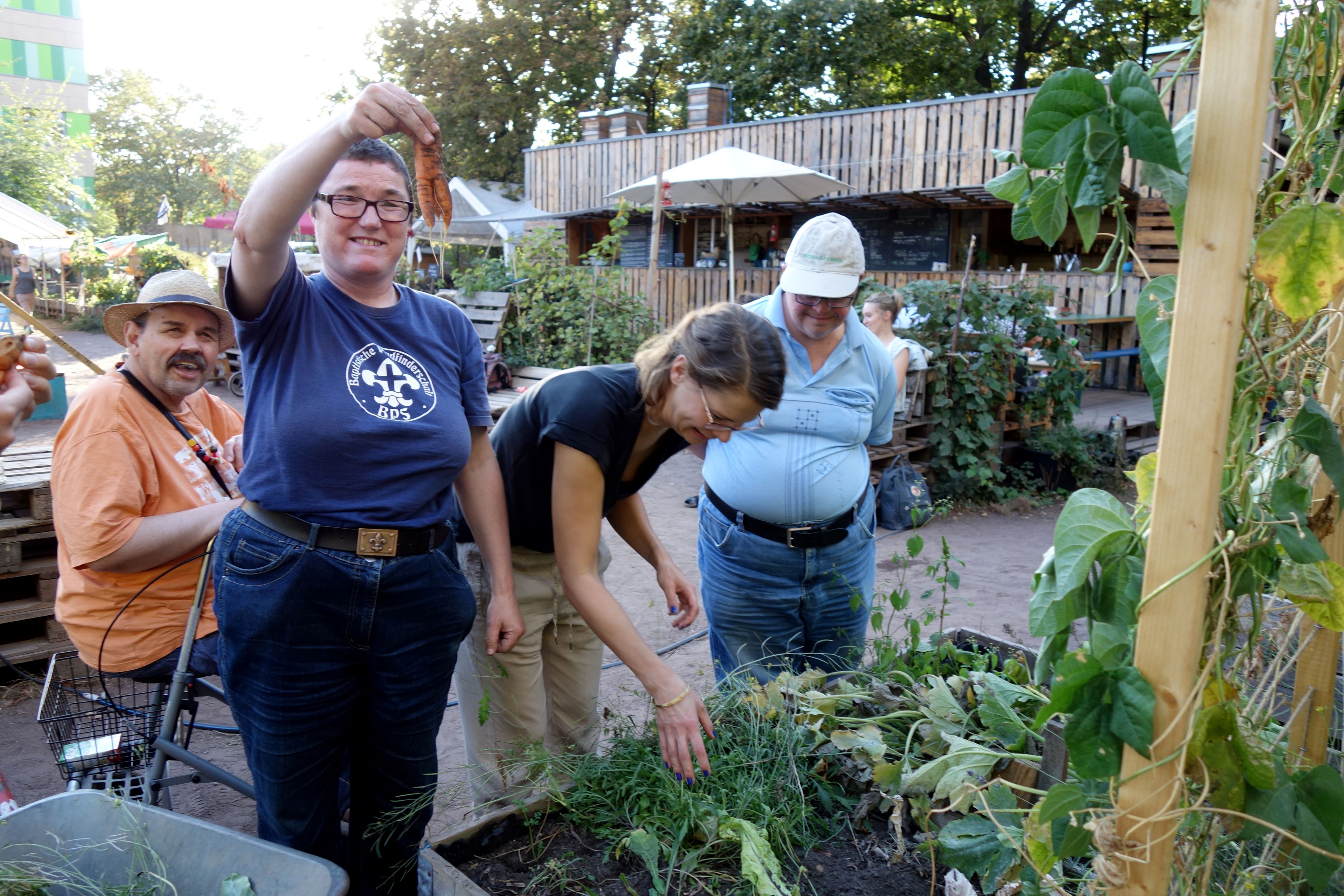 Vier Personen stehen vor einem Hochbeet. Eine Person hält eine Karotte hoch.