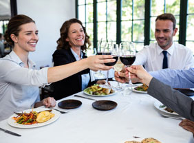 Kolleginnen und Kollegen, die beim Essen mit einem Glas Wein anstoßen