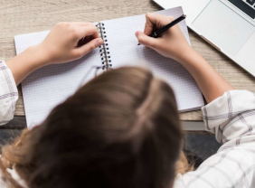 Junge Frau schreibt an ihrem Schreibtisch in ein Notizbuch