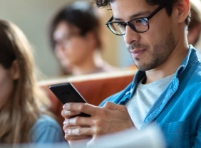 Junger Studierenden sitzt im Hörsaal und checkt sei Smartphone