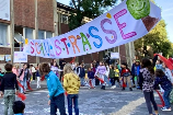 Das Bild zeigt spielende Kinder auf einer für Autos gesperrten Straße. Über der Straße hängt ein großes Banner mit dem bunten Schriftzug: "Spielstraße".