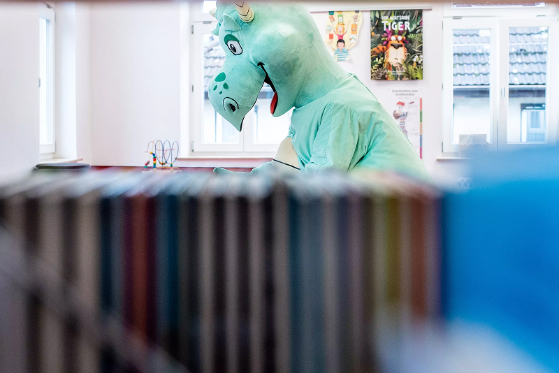 Person im Kostüm steht zwischen Bücherregalen in einer Bibliothek.