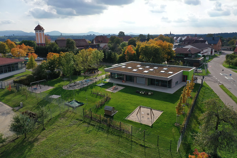 Luftaufnahme eines Kindergartens mit Spielplatz und umliegender Wohngegend.