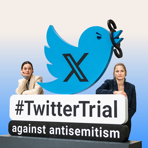 Das Bild zeigt zwei Personen, die links und rechts von einem Aufsteller des Twitter-Vogels (X) mit der Aufschrift „#TwitterTrial against antisemitism‟ stehen.