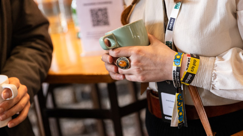 Nahaufnahme auf Hände, die einen Kaffeebecher halten. Um das eine Handgelenk liegen mehrere Eintrittsbändchen der c/o pop