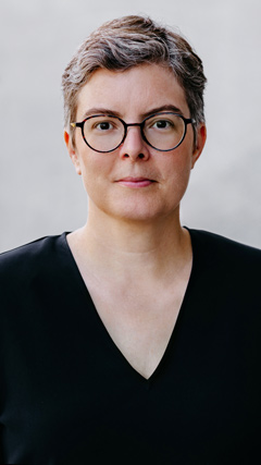 freundlich blickende Frau mit kurzen Haaren und Brille