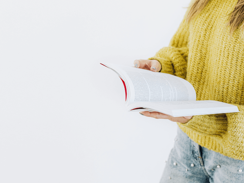 A woman in a yellow jumper holding an open book