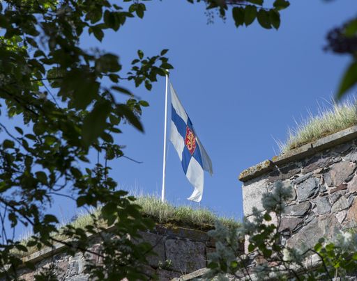 Suomen lippu liehuu muurien välistä kesäisenä päivänä.