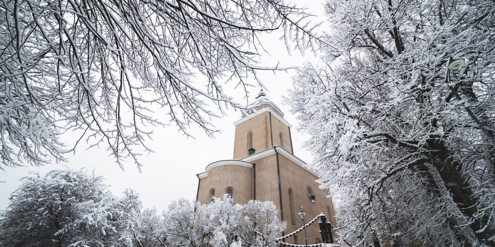 Kuvassa Suomenlinnan kirkko jota kehystää lumiset puiden oksat.