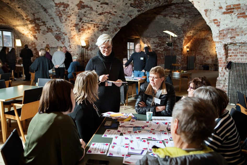 Ihmisiä kokoontuneena pöydän ympärille keskustelemaan.