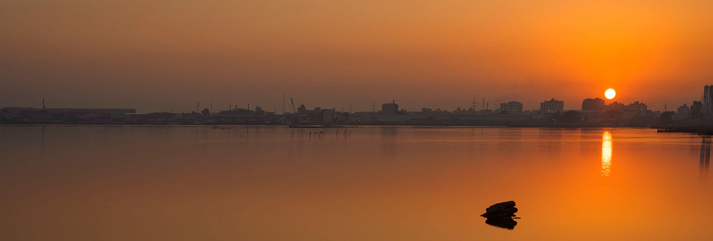 Rocks with reflections on calm water and beautiful sunrise over colorful sky with silhouette background, bahrain