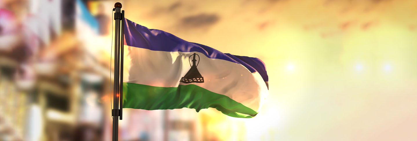 Lesotho flag against city blurred background at sunrise