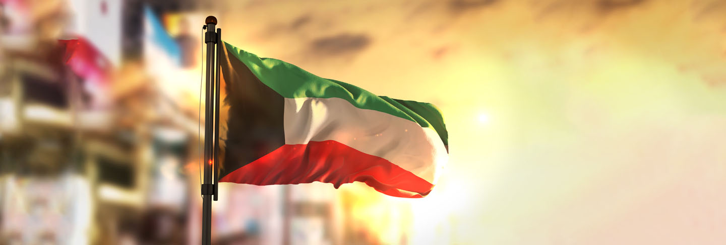 Kuwait flag against city blurred background at sunrise backlight