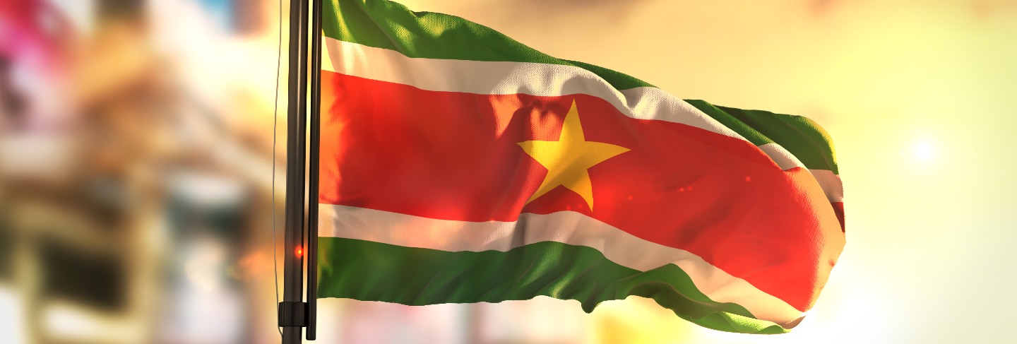 Suriname flag against city blurred background at sunrise backlight