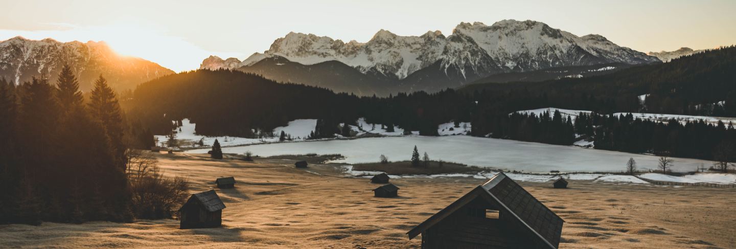 Long range shot of a valley with a hut house and tall snowy mountains