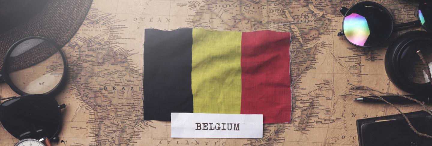 Belgium flag between traveler's accessories on old vintage map. overhead shot