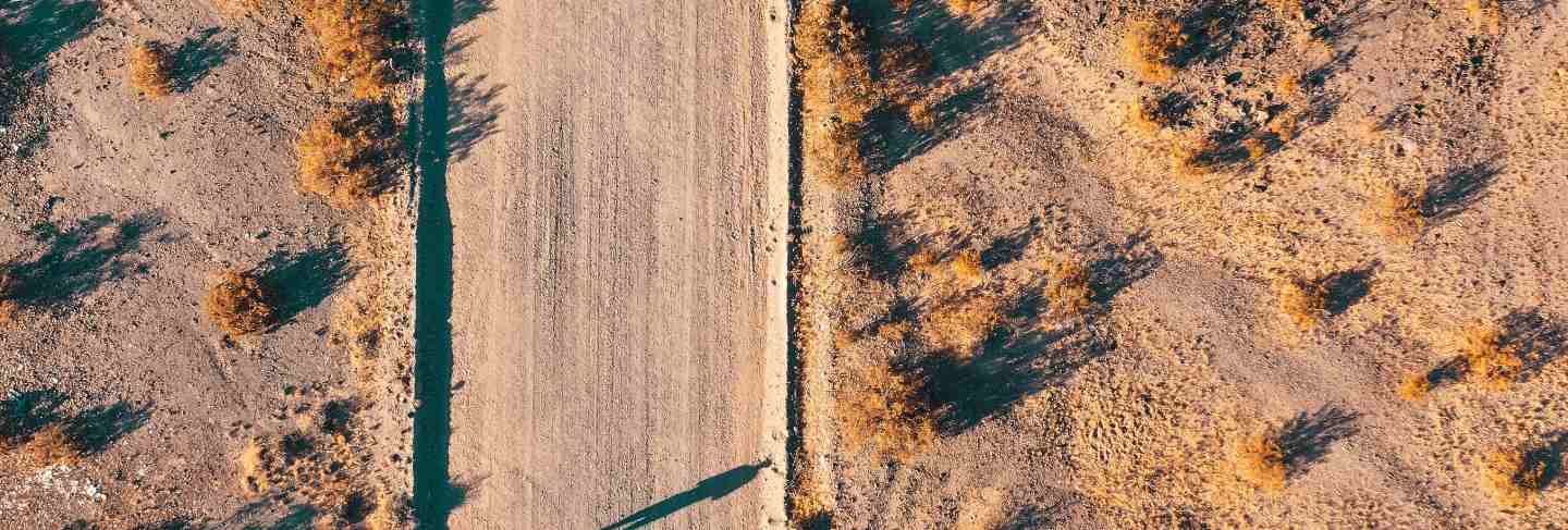 Overhead aerial drone shot of a narrow desert road with a car on the side of the road
