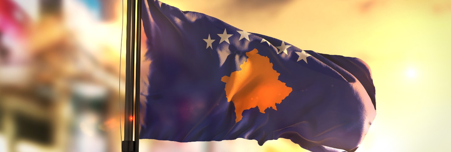 Kosovo flag against city blurred background at sunrise backlight