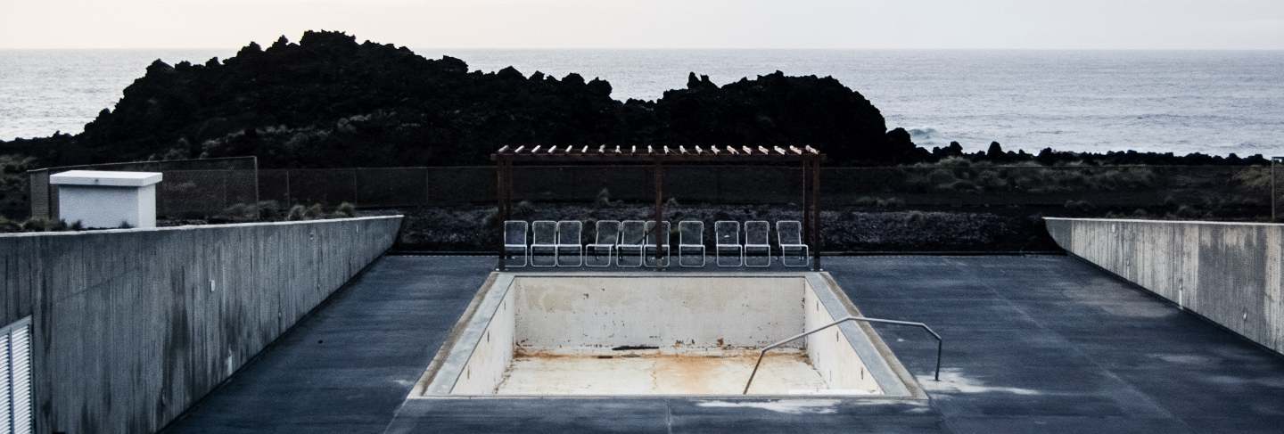 Empty pool with chairs near the cliff and a sea