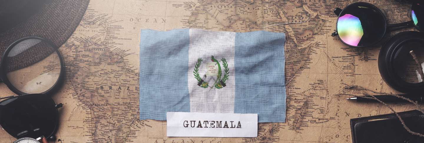 Guatemala flag between traveler's accessories on old vintage map. overhead shot