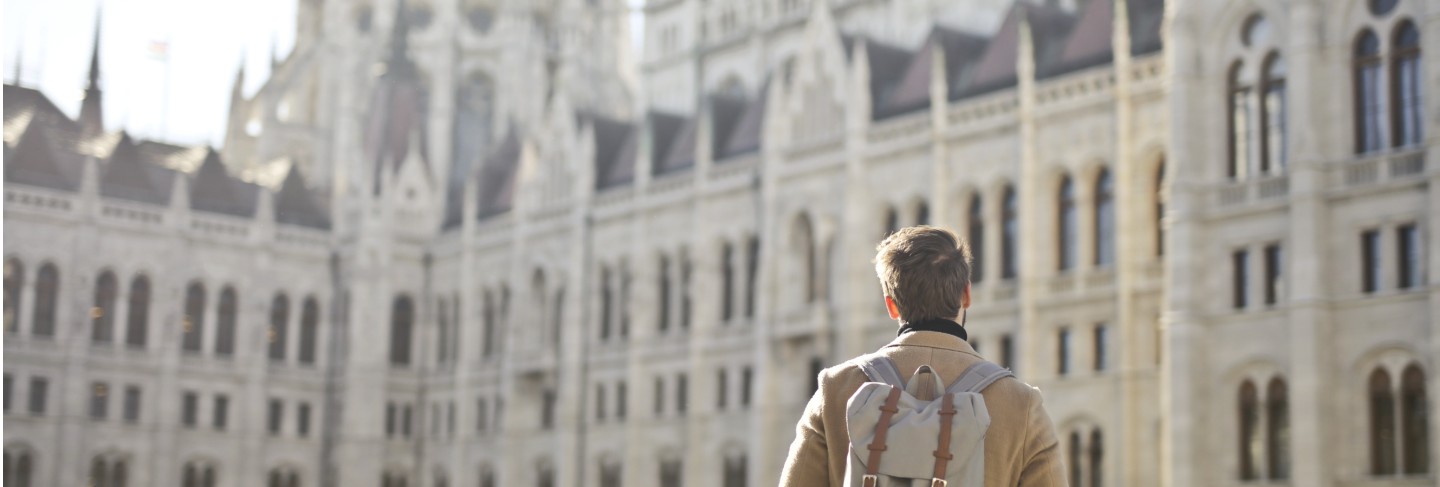Male wearing brown coat and backpack near hungarian parliament building in budapest