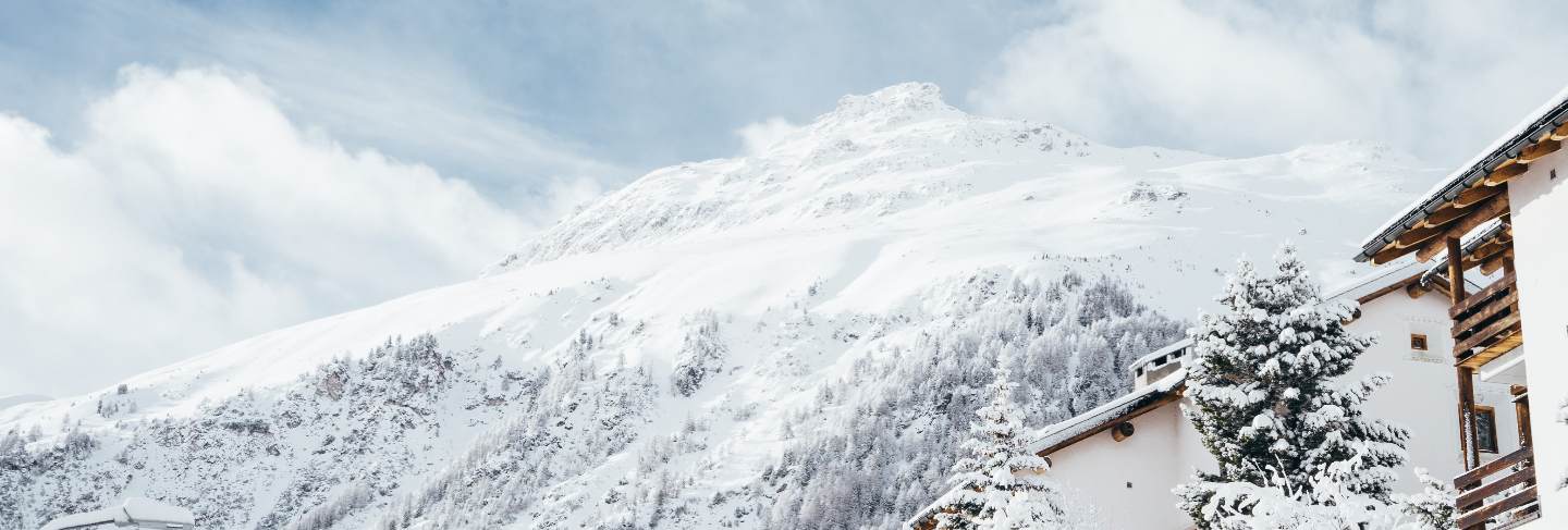 Wide shot of a white and brown house near trees and a mountain covered in snow
