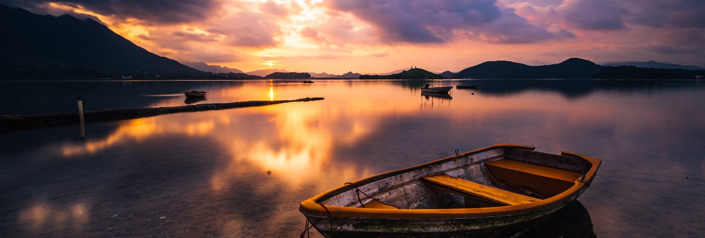 Beautiful shot of a small lake with a wooden rowboat in focus and amazing clouds in the sky