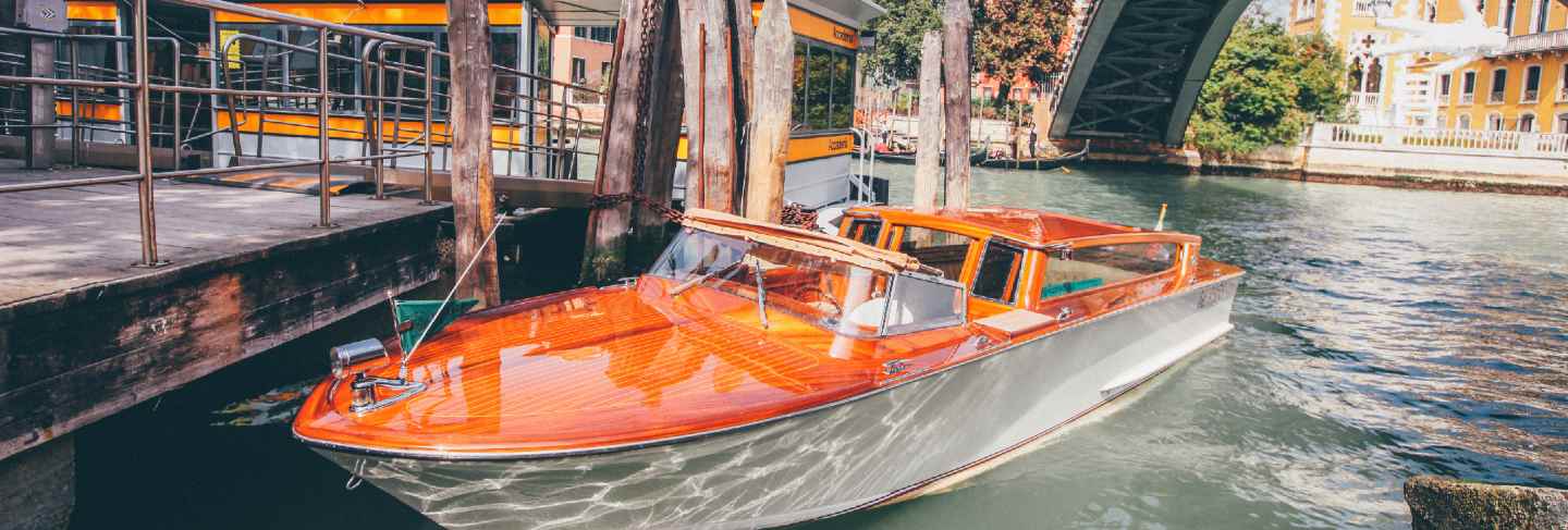 Orange waterway boat on a river under a bridge near buildings in venice, italy