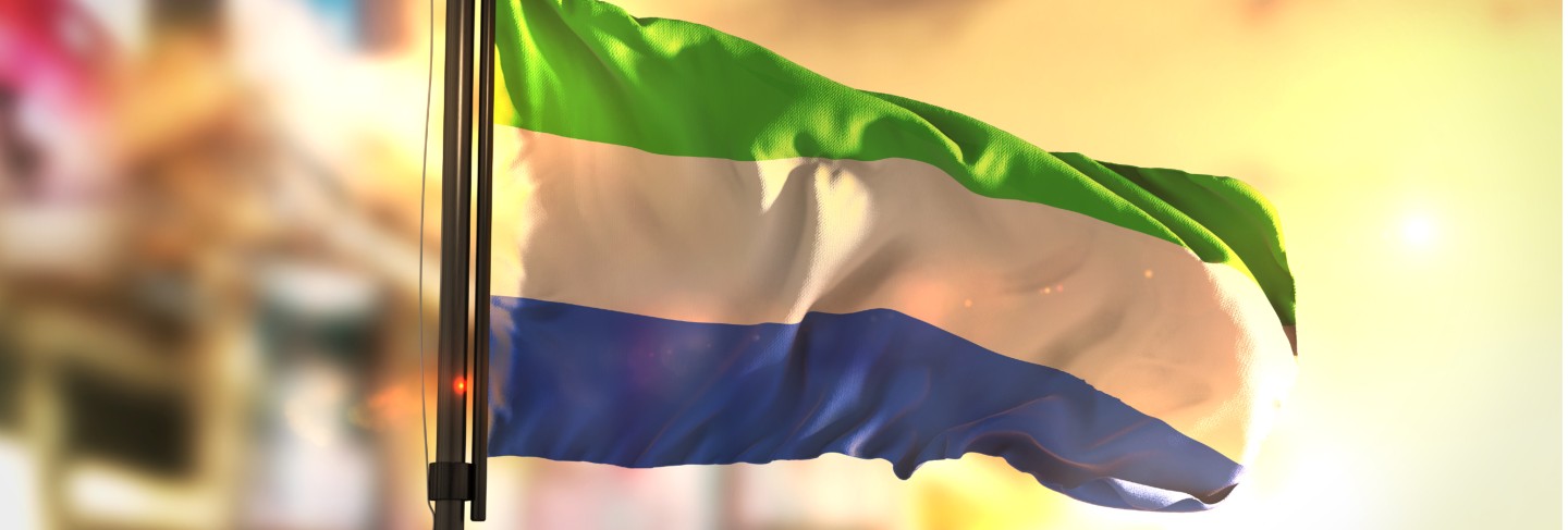 Sierra leone flag against city blurred background at sunrise backlight