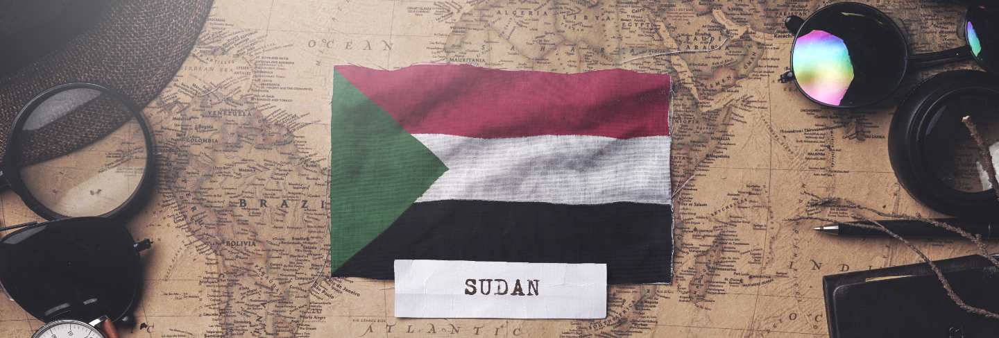 Sudan flag between traveler's accessories on old vintage map. overhead shot