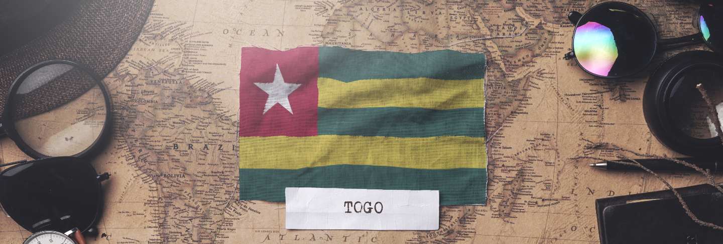 Togo flag between traveler's accessories on old vintage map. overhead shot