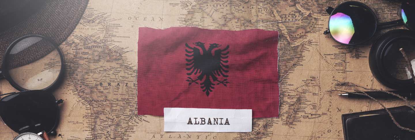 Albania flag between traveler's accessories on old vintage map. overhead shot