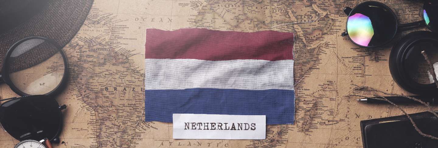 Netherlands flag between traveler's accessories on old vintage map.