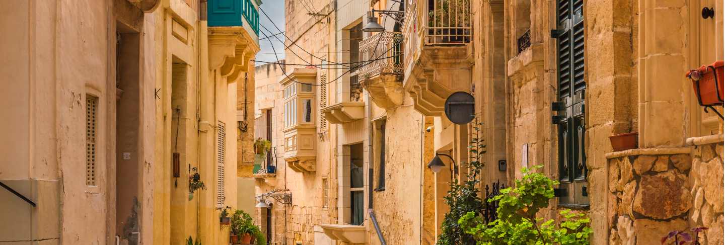 Old medieval street with yellow buildings, beautiful balconies and flower pots in birgu, valletta, malta Premium Photo