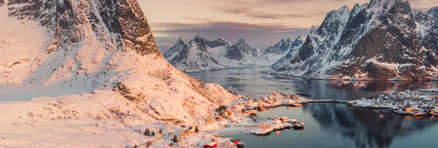 Aerial view of scandinavian village on coastline in snowy valley at sunset