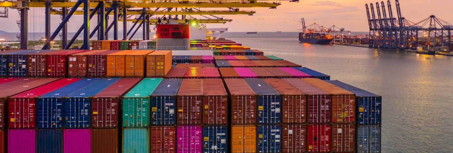 Container ship loading and unloading in deep sea port at sunset, aerial view of business logistic import and export