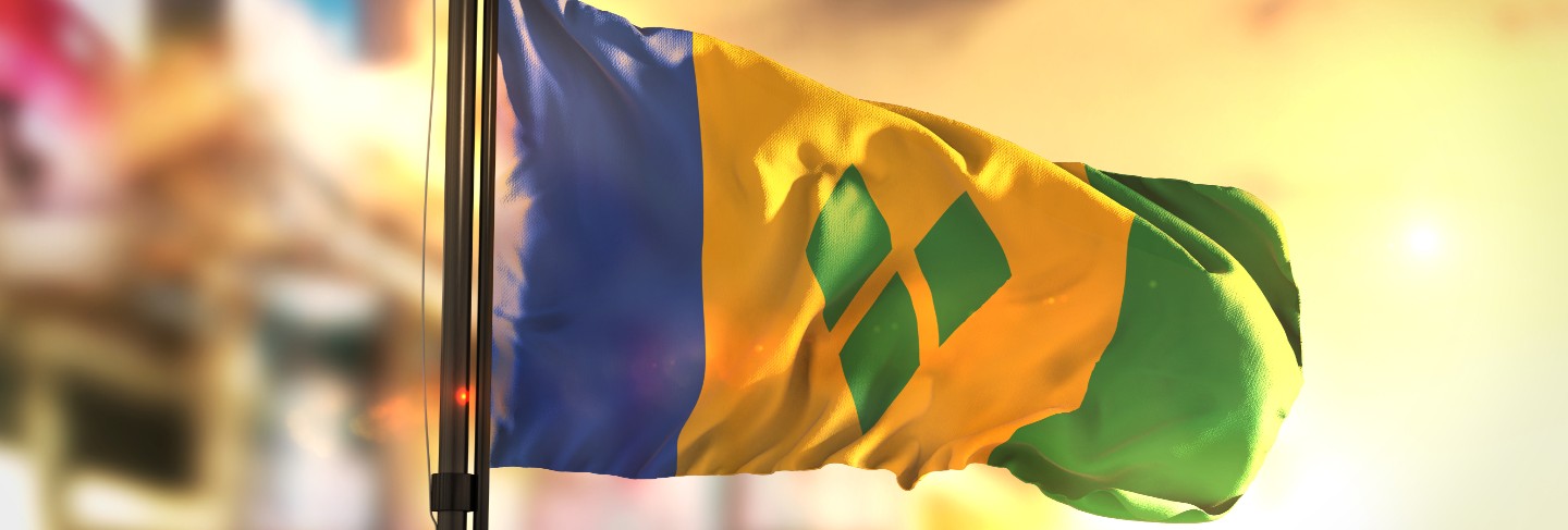 Saint vincent and the grenadines flag against city blurred background at sunrise backlight