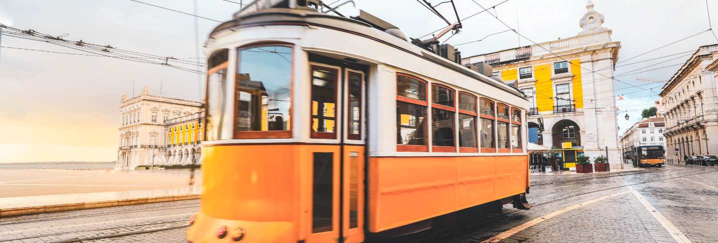 Selective focus on yellow building with blurred old traditional tram passing by city centre of lisbon, portugal.