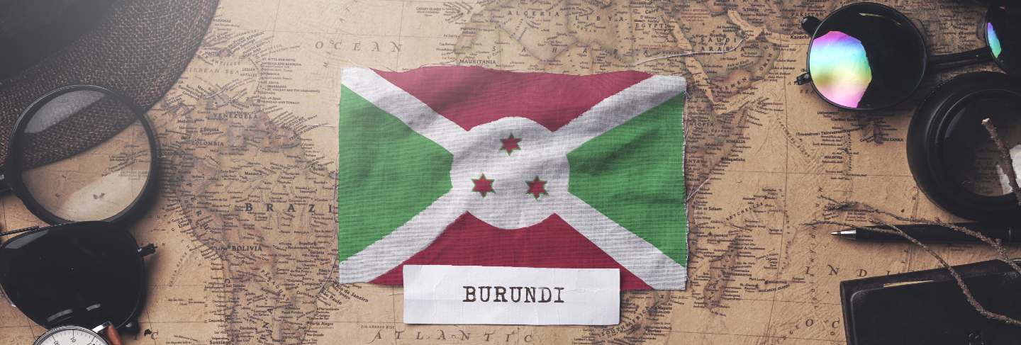 Burundi flag between traveler's accessories on old vintage map.