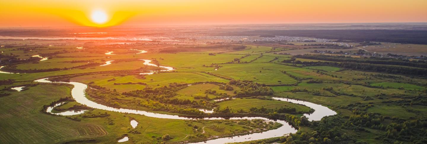 Beautiful summer sunset over a river with forests and fields
