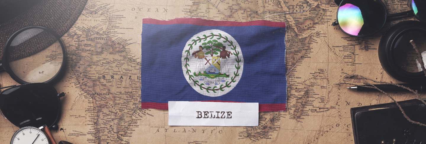 Belize flag between traveler's accessories on old vintage map.