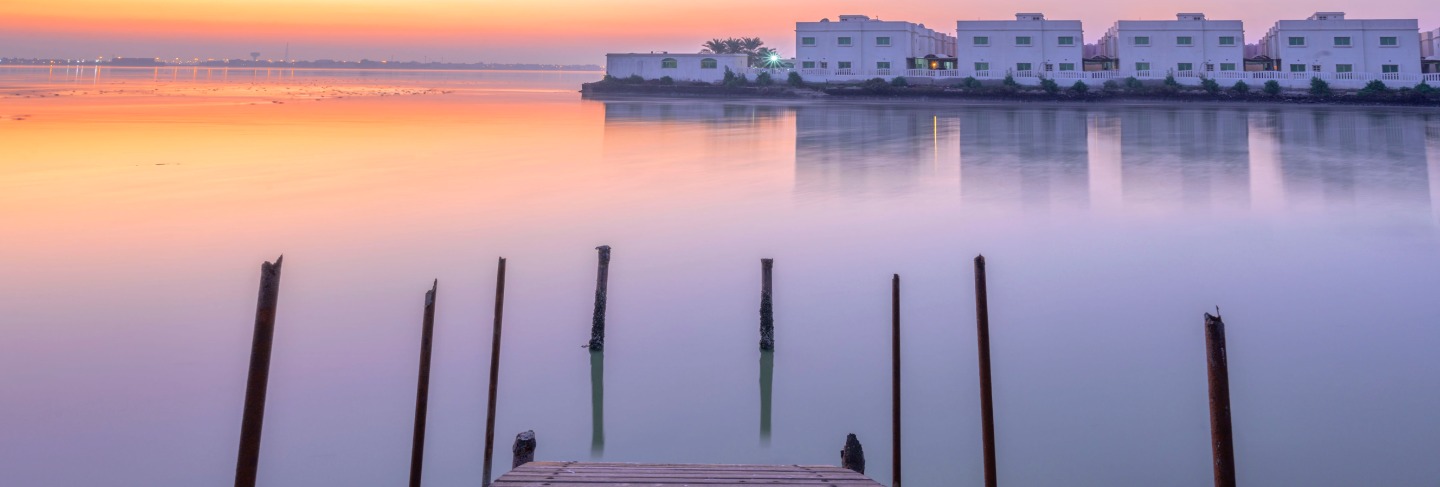 Wooden bridge out on the water over sunrise colorful sky with traditional local house in the island background,