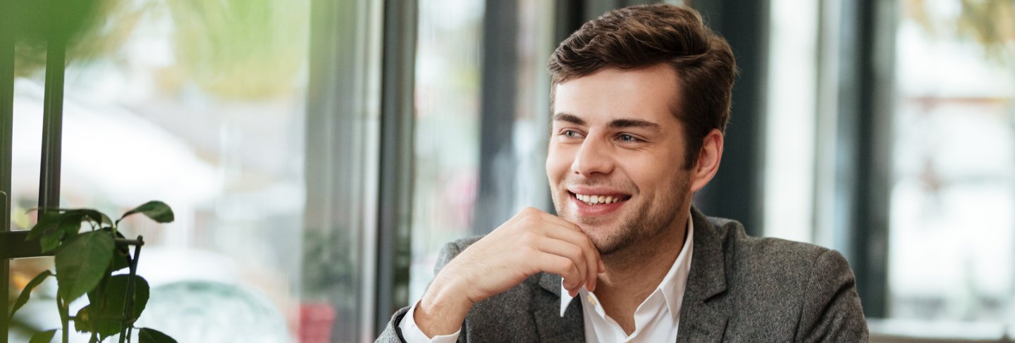 Smiling businessman sitting by the table in cafe with laptop computer and smartphone while looking away