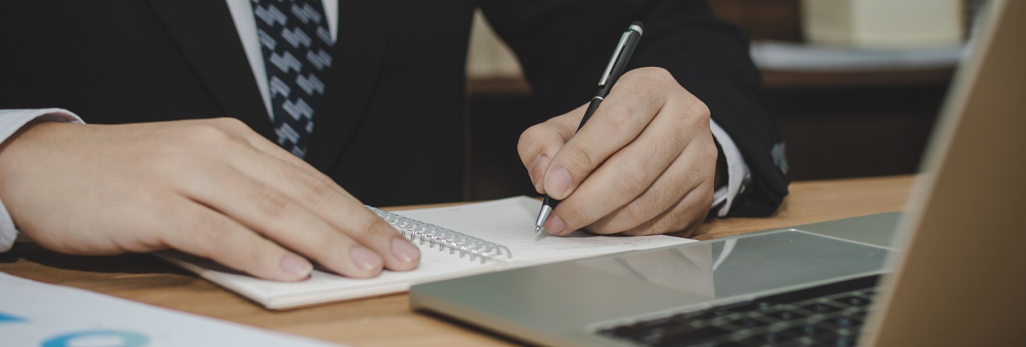 Attractive business man in black suit working and writing on document report on desk in meeting room at home office, investment, contract,