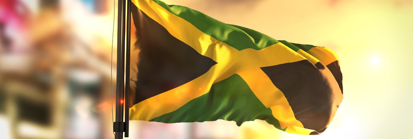 Jamaica flag against city blurred background at sunrise backlight