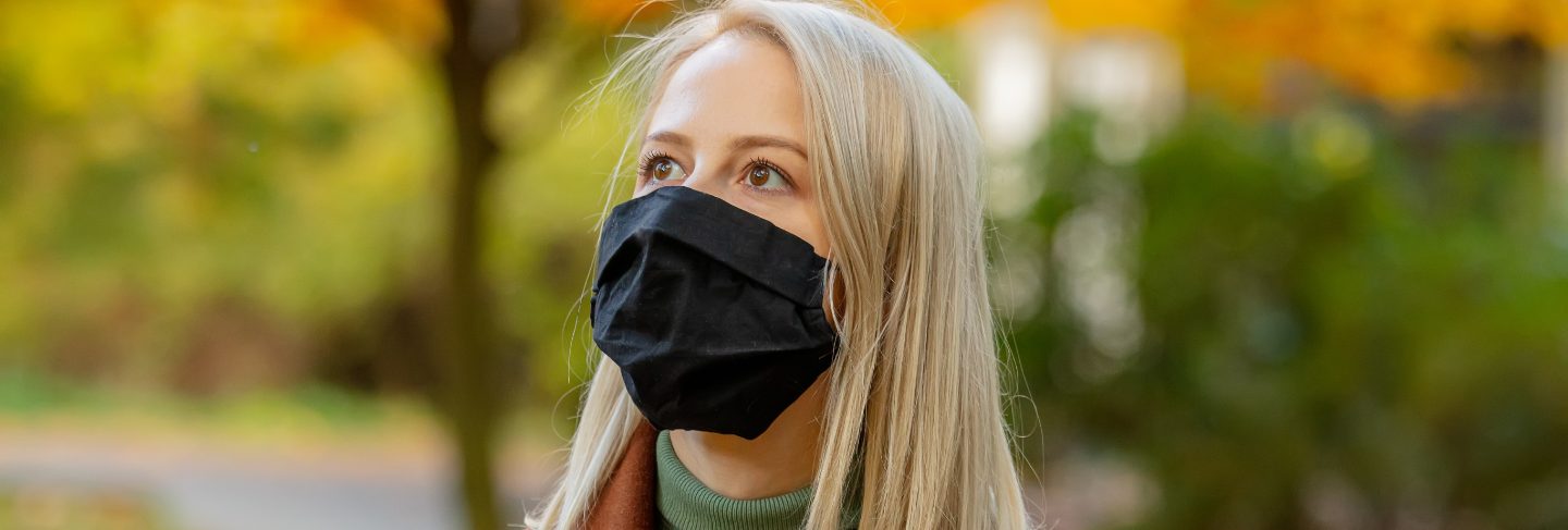 Style blonde in face mask and coat on autumn park with maples