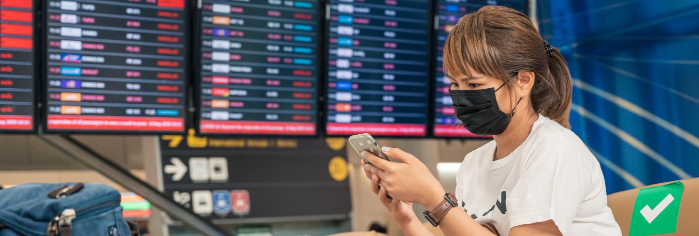 Asian female tourist wearing mask using mobile phone, searching airline flight status