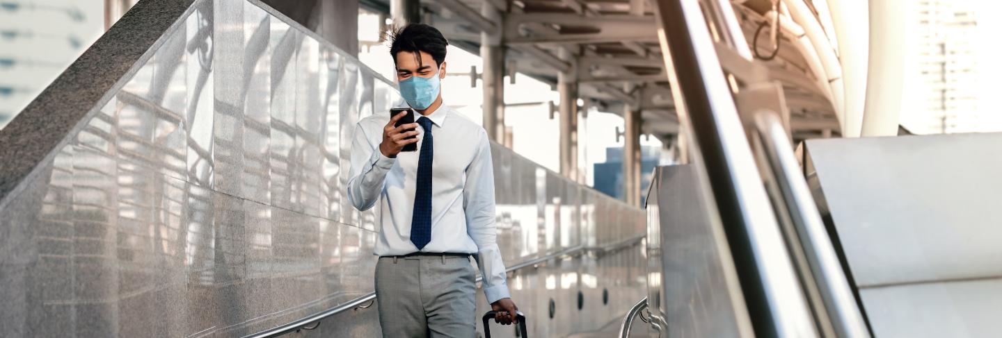 Young asian businessman wearing a surgical mask and using a smart phone while walking
