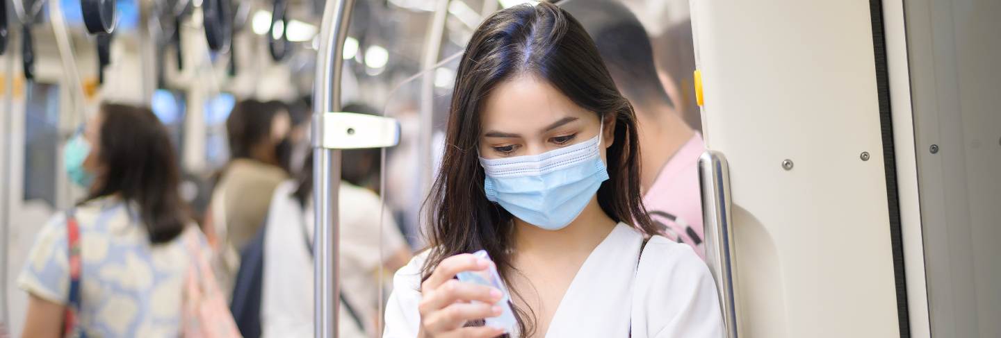 A young woman wearing protective mask in subway is using alcohol to wash hands, travel under covid-19 pandemic, safety travels, social distancing protocol