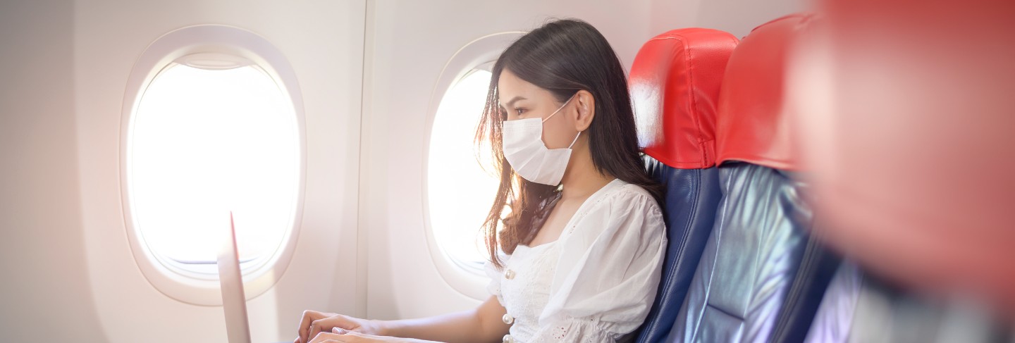 A young woman wearing face mask is using laptop onboard, new normal travel after covid-19 pandemic concept